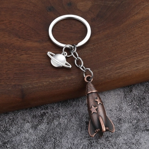 Detailed close-up of retro bronze rocket and silver Saturn charms on a sturdy metal keychain