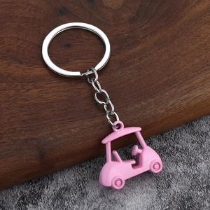3D pink metal golf cart keychain with silver ring on dark wood and grey ground