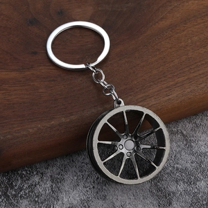Glossy black metal car wheel rim keychain with multi-spoke design on wood and stone background