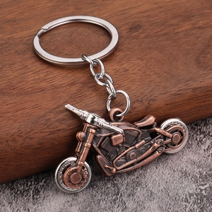 Vintage bronze motorcycle keychain with movable silver wheels on a rustic wood background