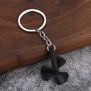 Black matte rotating windmill propeller keychain with silver ring on wooden and stone background