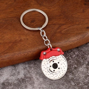 Close-up of a silver brake disc keychain with a bright red caliper on wood surface