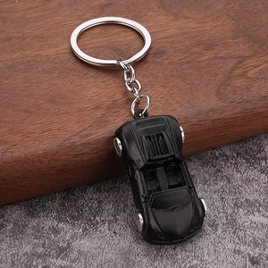 Detail of a sleek black convertible car keychain with silver wheels on a stone surface
