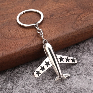 Silver metal aircraft keychain with star wings on dark wooden and stone background