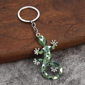 Close-up of green enamel gecko lizard keychain on dark wood and stone surface