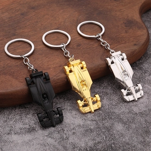 Three F1 racing car keychains in matte black, gold, and silver finishes on a wooden tray