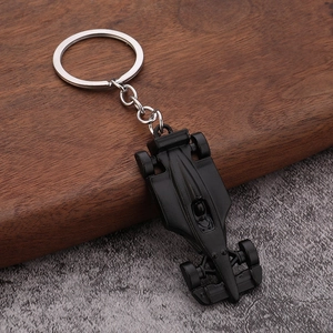 Detailed top view of matte black F1 racing car metal keychain on a stone and wood surface