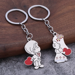 Matching couple keychains with cartoon boy and girl holding hearts on wood surface