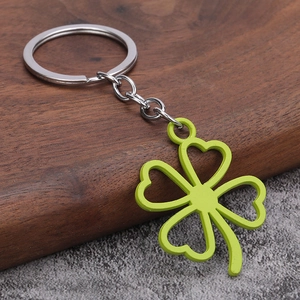 Minimalist green four-leaf clover keychain with silver metal ring on a rustic wooden background