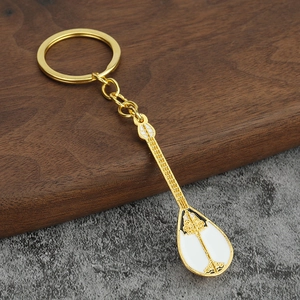 Close-up of golden Dombra musical instrument keychain with white enamel details