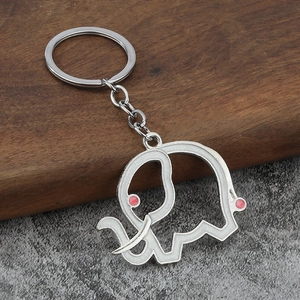 Minimalist silver elephant keychain with white enamel inlay and pink accents on stone background