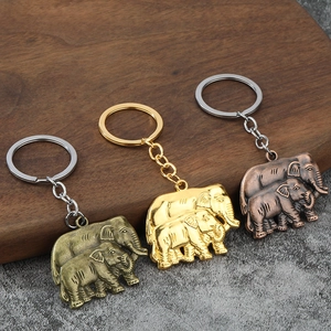 Three elephant-shaped alloy keychains in bronze and gold finishes on a rustic wood background