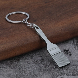 Detailed close-up of a silver metal brush pendant keychain on a wooden surface