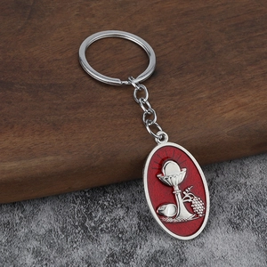 Religious metal keychain with red enamel chalice and bread relief on dark wood background