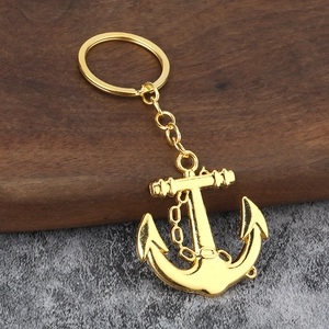 Polished golden metal anchor keychain with circular ring on rustic wooden and stone background