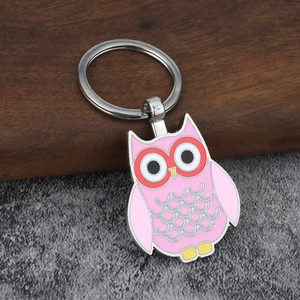 Pink enamel owl metal keychain with silver ring on a dark wooden and stone background