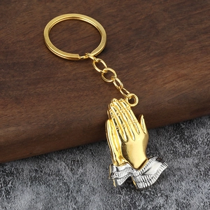 Golden and silver praying hands keychain on wooden and stone background