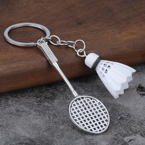 Miniature badminton racket and shuttlecock keychain with metallic finish on a wooden table