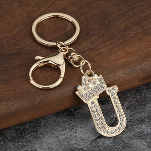 Détail d'un porte-clés lettre U doré avec couronne et strass brillants sur fond texturé