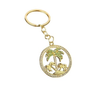 Golden coconut tree keychain with green and white crystals on a white background