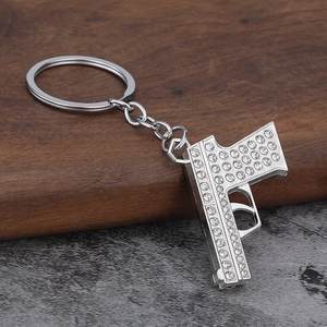 Hip hop style silver pistol keychain with sparkling white rhinestones on wood background