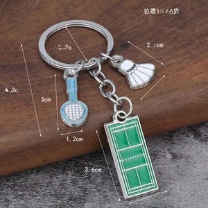 Detail showing badminton racket and shuttlecock keychain charms on dark wood background