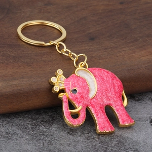 Pink enamel elephant keychain with gold crown and zinc alloy texture on wooden base