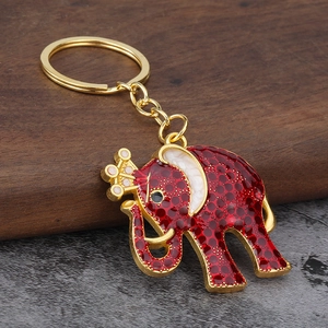 Detailed view of red enamel elephant keychain with gold crown on dark wood base