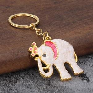 Detailed view of golden elephant keychain with white enamel and pink crown on wood base