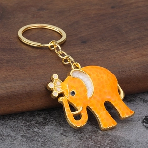 Orange Thai elephant keychain with gold crown and metal ring on dark wood surface