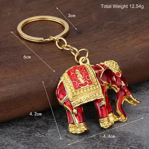 Enamel Thai elephant keychain with intricate golden patterns on a rustic wooden stand