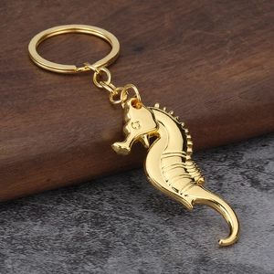 Polished golden seahorse metal keychain with intricate engraving on a textured background
