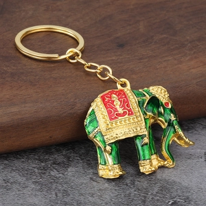 Exquisite golden elephant keychain with green enamel and red pattern on rustic wood background