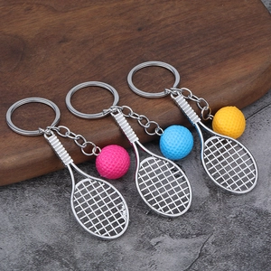 Mini tennis racket and ball keychain set in pink, blue, and yellow on wooden base