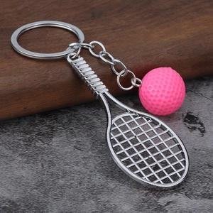 Detail of pink tennis ball and silver racket keychain on wooden and stone surface