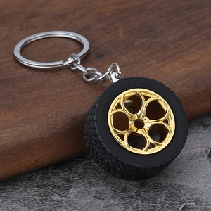 Detail of a car tire keychain with a black rubber wheel and golden hub on a textured background