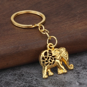 Golden elephant keychain with intricate hollow carvings on dark wood and stone background