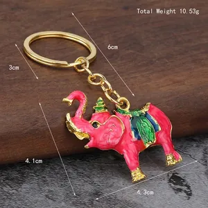 Pink elephant keychain with colorful enamel pattern and gold finish on dark wood background