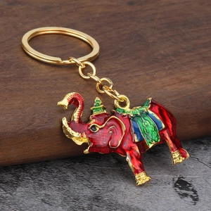Red enamel elephant keychain with gold crown and decorative saddle on wood background