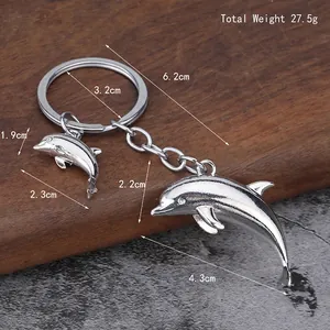 Zilveren metalen dolfijn sleutelhanger met twee hangers op hout- en steenachtergrond