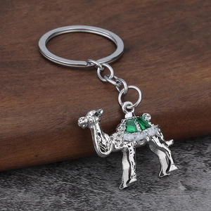 Detailed close-up of a silver camel keychain with green enamel inlay on a dark surface