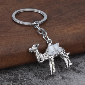 Close-up of a silver camel keychain with white enamel saddle on a textured base