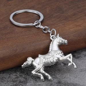 Close-up of a silver running horse metal keychain with saddle detail on dark wood surface
