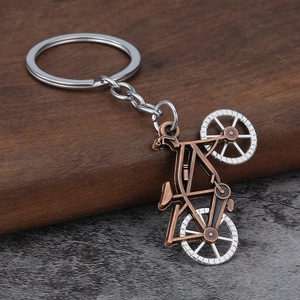 Vintage metal alloy bicycle keychain with bronze and silver finish on a rustic wooden stand