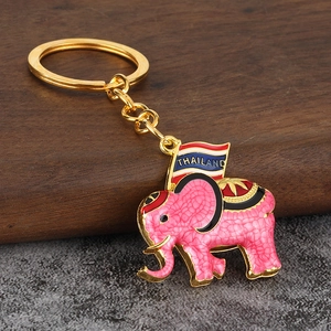 Macro detail of a pink Thai elephant keychain with a Thailand flag on a wooden block