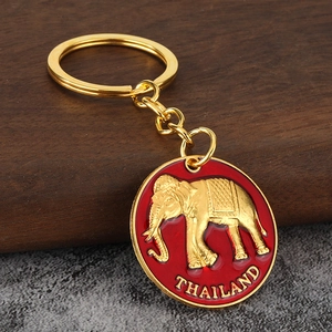 Golden elephant keychain with red enamel pendant featuring Thailand relief on wood background