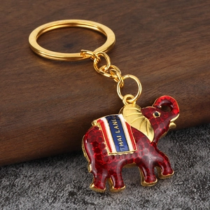 Golden elephant keychain with red enamel and blue Thailand banner on wooden base