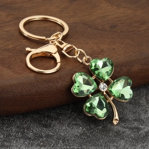 Golden clover keychain with green heart-shaped crystals and lobster clasp on dark wood