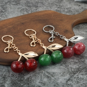 Fashionable resin cherry keychains with glitter and metal leaves on wooden tray
