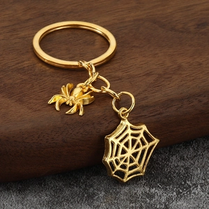 Golden spider and web keychain charms displayed on a rustic wood block background